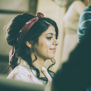 Latina beauty in her early twenties. Soft smile. Dark brown hair styled with maroon headband. Close-up, blurred background