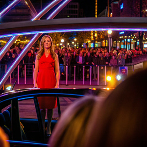 Jennifer Aniston at the premiere of her new film. Dressed in a vibrant red dress. Crowds and flashing lights in background.