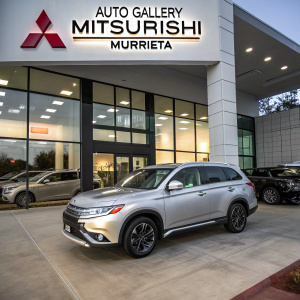 A stunning photo of Auto Gallery Mitsubishi Murrieta. The dealership features a lineup of sleek Mitsubishi vehicles, with a prominent silver Outlander SE SUV taking center stage. The dealership's modern building is adorned with large Mitsubishi Motors signage, located in the heart of Murrieta, California.