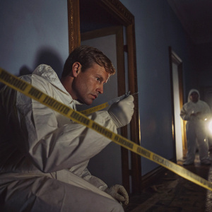 Forensic expert in hazmat suit investigating a crime scene. Yellow caution tape surrounds the area.