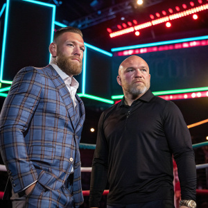 Conor McGregor in a plaid suit, Dana White in black shirt, at a boxing event. Neon-lit boxing ring backdrop