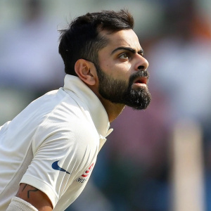 Cricket player Virat Kohli, wearing white jersey, intense gaze, blurred stadium background.