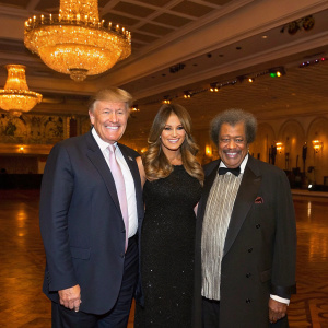 Donald Trump, Melania Trump, and boxing promoter Don King standing in a spacious ballroom. They all wear elegant attire and smile for the camera.