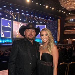Jason Aldean and Brittany Kerr, dressed in formal attire, attending a Grammy Awards ceremony. A lavish stage backdrop with LED screens.