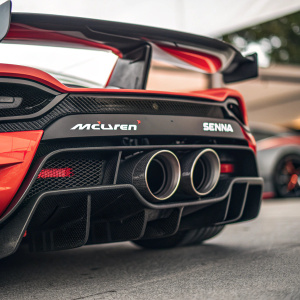Close-up shot of McLaren Senna's exhaust system. Red and black colors highlight the sleek design. Prominent McLaren logo. Unique aerodynamic pipes contrast sharply against each other.