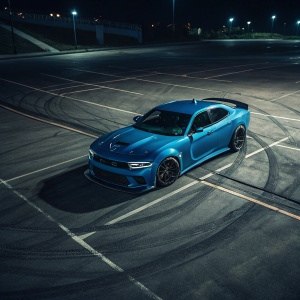 A sleek blue Dodge Charger SRT Hellcat Widebody parked in an empty parking lot at night. Tire marks visible on the dark asphalt. Shot from above, highlighting the car's wide body and aggressive front end design.