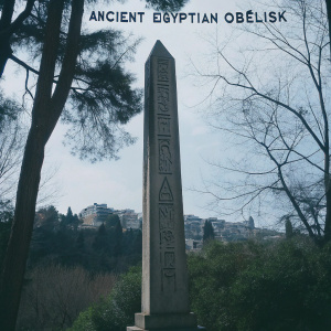 An ancient Egyptian obelisk, etched with arcane hieroglyphs, looms in a lush forest clearing. Its weathered facade reaches towards the azure sky, its peak touching the clouds. Beyond, an ancient city of towering spires and stone fortresses fades into the horizon, their mysteries hidden in the breeze. Wisps of cirrus clouds paint the heavens, a scene of timeless beauty.
