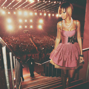 Rihanna, at the 2010 Kids' Choice Awards. Blonde hair with dark roots. Wearing a pink dress with layered skirt and pearl necklace. Crowded venue, bright lights