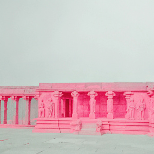 Realistic photograph of Airavatesvara Temple's Nataraja mandapa in Darasuram, Tamil Nadu. The mandapa features detailed stone sculptures and columns. Statues of various sizes depict figures in traditional attire. Intricate carvings in shades of orange and brown adorn the architecture.
