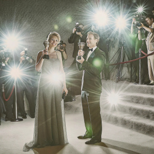Emma Thompson and James McAvoy at a glamorous awards ceremony. They both hold trophies and champagne glasses. Crowded event with lights and cameras