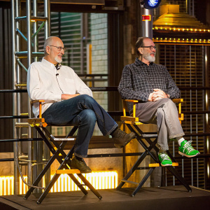 James Cromwell and Jon Cromwell attending a press conference for the Heineken Awards. They are both dressed casually. One wears a white shirt and the other a black checkered shirt. The backdrop features the Heineken logo.