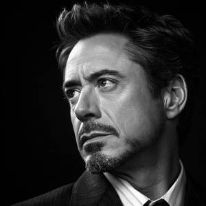Close-up portrait of Robert Downey Jr. as Tony Stark from Iron Man series. Black and white, dark background, detailed facial features, serious expression, stubble, suit