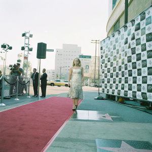 AnnaSophia Robb, in a stunning floral white dress, walking on the Hollywood Walk of Fame during the Young Hollywood Awards event. Red carpet with black and white checkered backdrop featuring award logos.