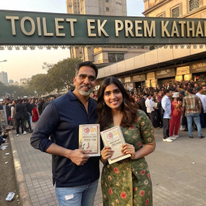Bhumi Pednekar and Akshay Kumar, posing proudly with books on the bustling streets of Mumbai, promoting their film 'Toilet: Ek Prem Katha'. Crowds of fans and media in the background.