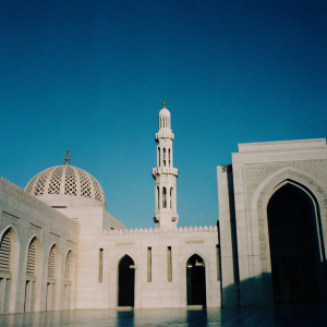 Sultan Qaboos Grand Mosque in Muscat, Oman. Majestic building with white stone and intricate designs. Clear blue sky, emphasizing the grand facade.