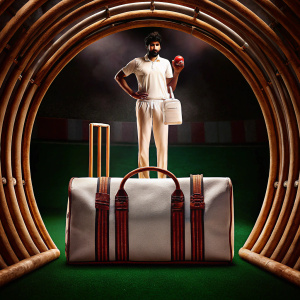 Promotional photo of Jasprit Bumrah on a white bag with red highlights. Green grass background.