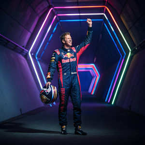 Sebastian Vettel, in celebratory pose, wearing racing suit with Red Bull logo. Backdrop is a dimly lit tunnel with neon lights.