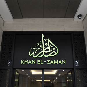 The Khan El-Zaman logo, a sleek, modern design featuring Arabic calligraphy. Neon green font against a black background.