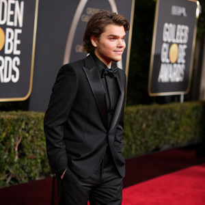Emile Hirsch, young actor, in a sleek black tuxedo, posing solo on the carpet at the Golden Globe Awards. Dark and dramatic backdrop