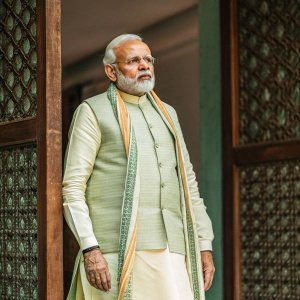 Narendra Modi, the Indian Prime Minister, in traditional attire. Dark brown backdrop with intricate patterns.