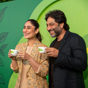 Kareena Kapoor and Vikram Grover at a Tetley Green Tea launch event. They stand in front of a vibrant green backdrop. Both are smiling, holding small tea cups.