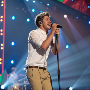 Niall Horan, formerly of One Direction, singing at the Teen Choice Awards. Wearing a white shirt and khaki pants, he performs on stage.