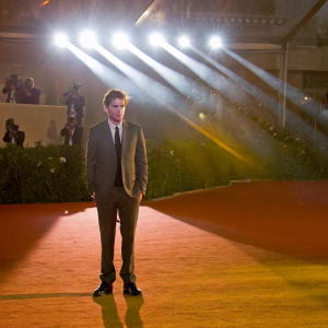 Robert Pattinson at Venice Film Festival, standing solemnly under bright spotlights.
