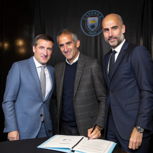 Ferran Soriano, Txiki Begiristain, and Pep Guardiola at Manchester City's signing ceremony. Wearing suits. Dark background