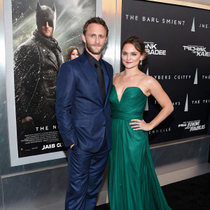 Josh Stewart and Deanna Brigidi-Stewart at the New York City Film Festival premiere. Josh in a sleek navy blue suit. Deanna in a floor-length emerald green gown. Promotional backdrop for 'The Dark Knight Rises'