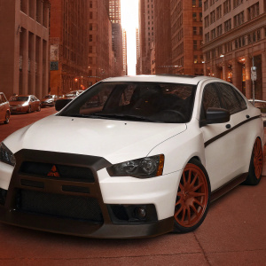 Customized Mitsubishi Lancer Evolution X, with distinct red rims and matte black grille. The car is parked in a bustling city street surrounded by tall skyscrapers.