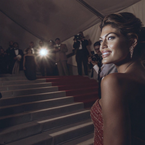 Eva Mendes at the Met Gala, glammed up in a sparkling red gown, posing confidently on the red carpet amidst a crowd of fashion enthusiasts.