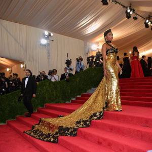 Nicki Minaj at the Met Gala. Stylized red carpet with high heels. Long, gold and black sequined gown