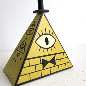 Close-up view of Bill Cipher figure from Gravity Falls. Triangular shape, yellow with black details. Symbols and an eye are clearly visible. Set against a plain white background.