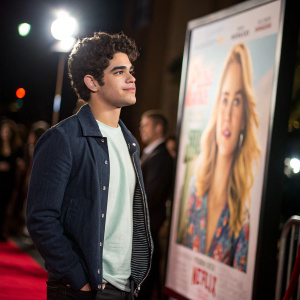 Emery Kelly at the Netflix 'Alexa & Katie' premiere. Dressed casually, standing in front of a large movie poster in a close-up shot. Background blurred, spotlight on him.