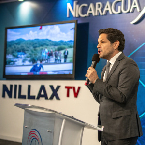 Luis González Posada in a sleek grey suit addressing the camera at a press conference. Behind him, a large screen displays breaking news about Nicaragua. Willax TV logo prominently displayed.
