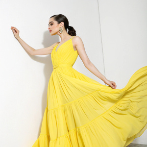 Sofia Carson, stunning in a vibrant yellow dress, standing solo against a plain white background, showcasing her elegance and presence.