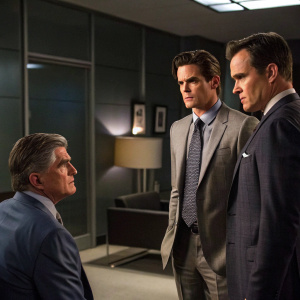 Treat Williams, Matt Bomer, and Tim DeKay in a tense standoff scene from White Collar. Set in a dimly lit, modern office. Wearing business suits with concerned expressions.