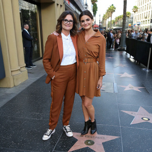 Ally Sheedy and Sofia Black-D'Elia at the Hollywood Walk of Fame. Both in brown outfits, Ally in a blazer with white blouse and sneakers, Sofia in a high-waisted belted dress with black heels. Crowded street backdrop