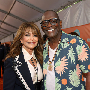 Paula Abdul and Randy Jackson grinning at the Nickelodeon Kids' Choice Awards. Paula in black and white outfit, Randy in Hawaiian shirt. Tent-like backdrop.