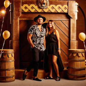 Jai Courtney and Mecki Dent attending the special screening event. Jai in a black and white patterned shirt and a hat. Mecki in a black dress. Lionsgate-themed backdrop with event banners.