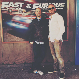 Aaron Paul and Bryan Cranston standing in front of an advertisement board promoting the film 'Fast & Furious'.