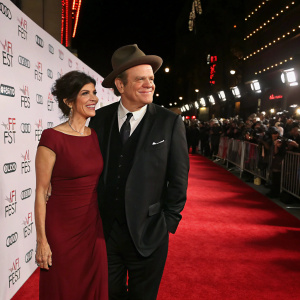 Alison Dickey and John C. Reilly walking the AFI Fest red carpet. Alison in maroon dress, John in black suit and hat.