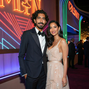 Dev Patel and Olivia Munn at an exclusive gala event. They are posing in front of a vibrant, neon-lit backdrop.