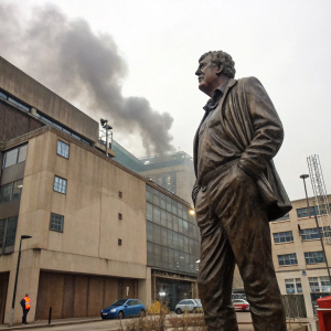 Life-sized bronze statue of Jeremy Clarkson outside the BBC studios. He is depicted with a stern expression. A gritty, industrial backdrop