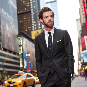 Harry Treadaway, bearded actor in a sleek black suit with dotted tie, promoting new Sky Atlantic series. A bustling cityscape backdrop.