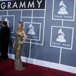 Hilary Duff at the Grammy Awards, dressed in a gold sequined gown. Confident pose, red carpet. Grammy logo backdrop.