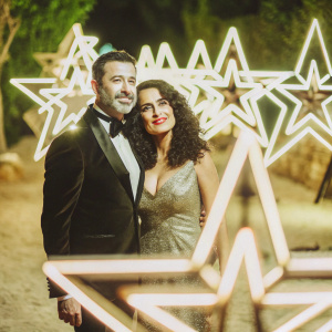 Jimmy Kimmel and Salma Hayek, two celebrities, posing for a photograph at a star-studded gala. Jimmy, with his stubble and sharp jawline, stands close to Salma, her hair a cascade of dark curls. The event backdrop is a shimmering array of stars.