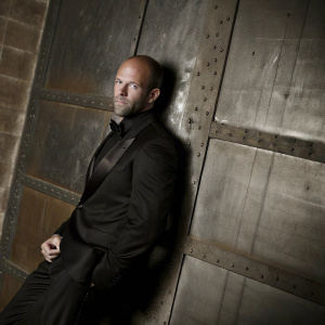 Jason Statham, in a sleek black tuxedo, posing against a sleek, metallic backdrop. Close-up shot highlighting his chiseled features and the luxurious fabric of his attire.