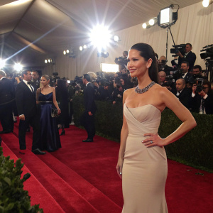 Olivia Munn at the Met Gala. Elegant evening gown, standing amidst a sea of celebrities. Bright stage lights and camera flashes