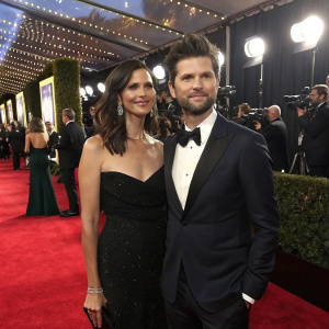 Adam Scott and Naomi Scott at a glitzy awards show. They stand on a lavish red carpet surrounded by flashing cameras.